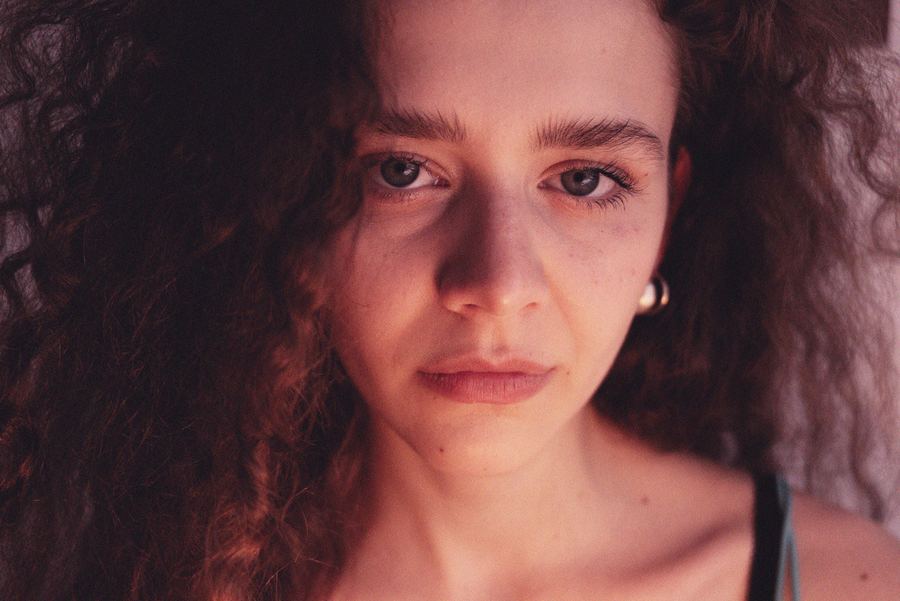Close-crop portrait, dark curly hair, direct gaze, small hoop earring, warm side lighting.