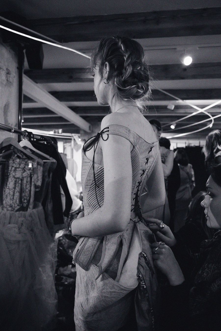 Backstage, the laced corset back of a structured dress is fastened on a model with braided hair.