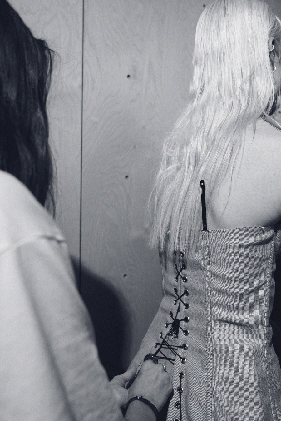 Backstage, a model's laced denim corset top is fastened, her long blonde hair falling over bare shoulders.