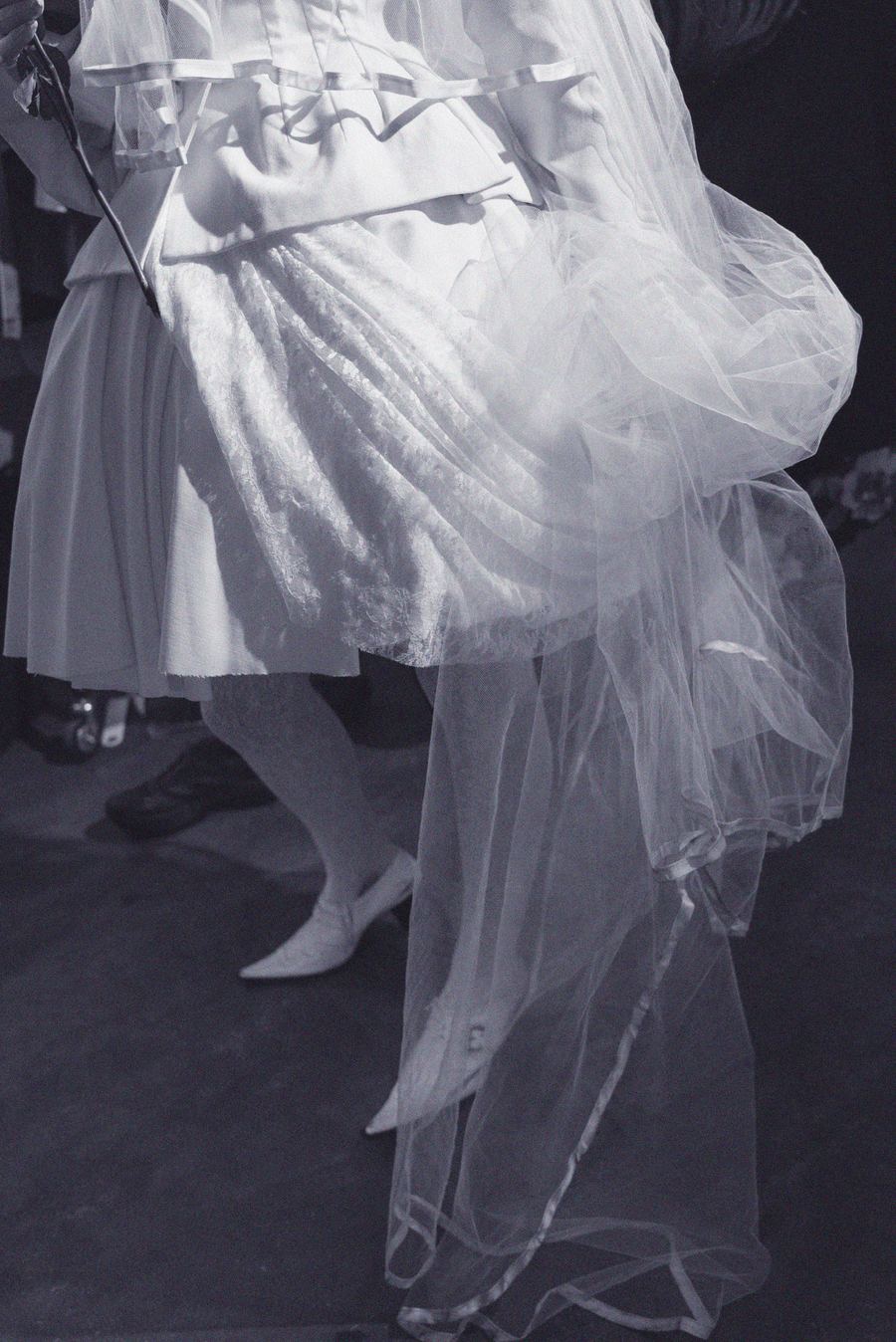 Close-up of a white lace and tulle skirt with a full, gathered tulle overlay, worn with pointed pumps.